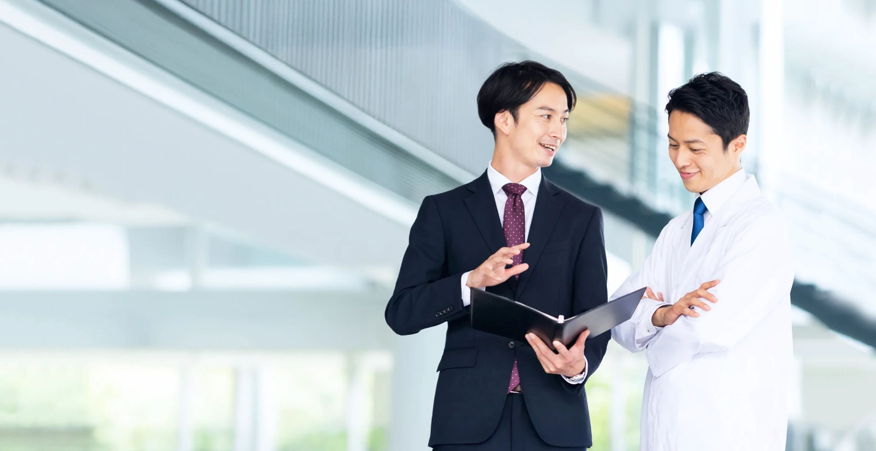 白衣とスーツをきた男性が資料をみながら話している様子